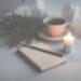 A journal and candle sit on a desk with a green flower and a coffee, the image is hazy to depict thoughtfulness, and the role of writing about your fibromyalgia in your battle to gain some normality again.