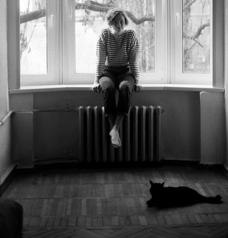 a lady sits in a large window with a cat sat on the floor in front of her